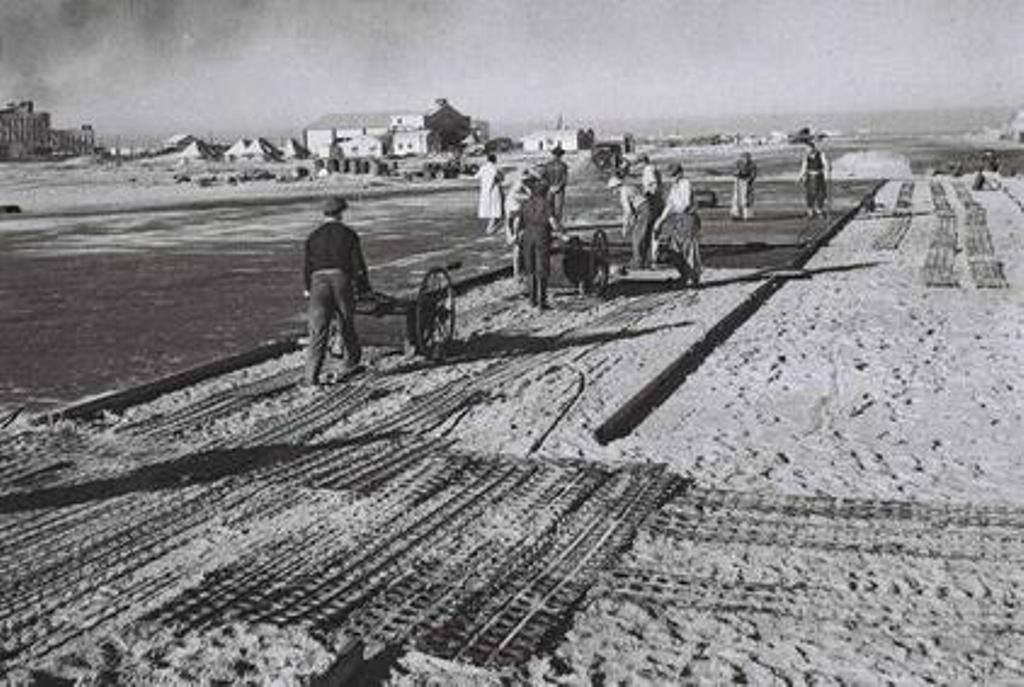 פועלים סוללים את מסלול ההמראה של שדה התעופה שדה דב. ברקע - בניית תחנת רידינג 1938 (צילום: זולטן קלוגר, פיקוויקי)
